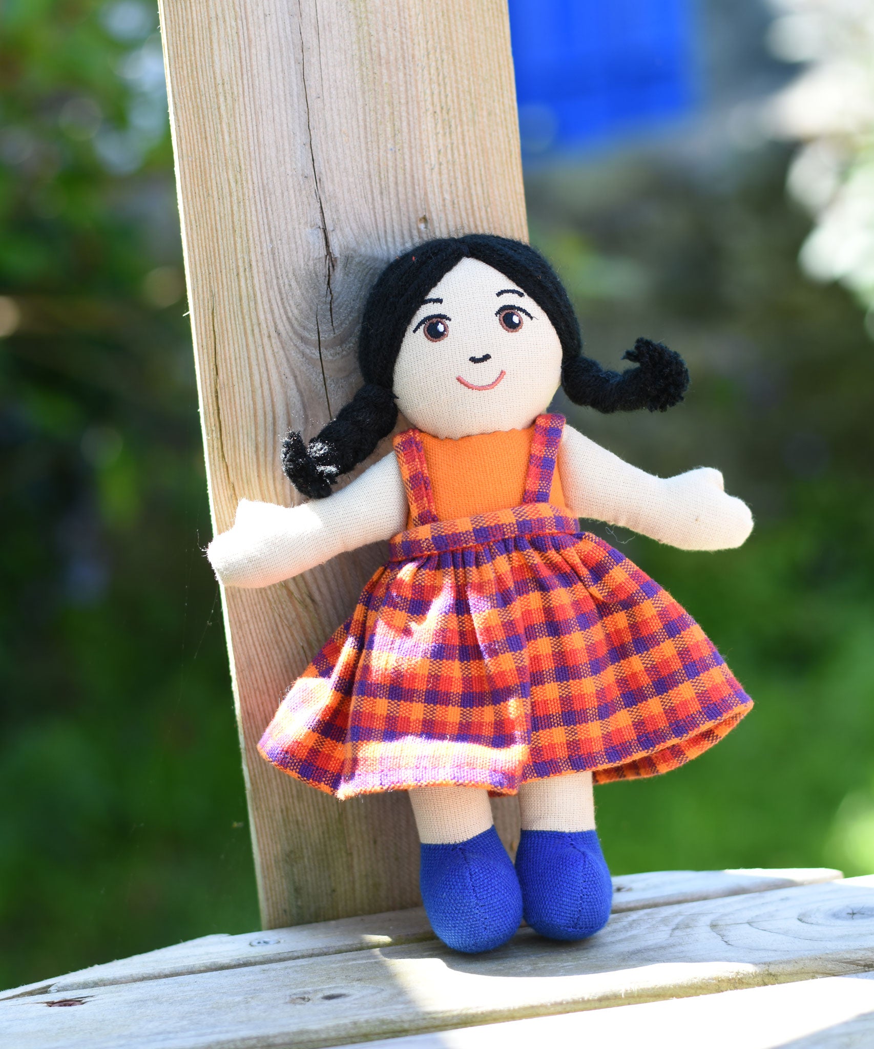 A A Lanka Kade Girl Doll with White Skin and Black Hair leaning against a wooden fence post outdoors.
