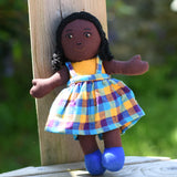 A Lanka Kade Girl Doll with Black Skin and Black Hair leaning against a wooden post outdoors.