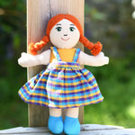 A Lanka Kade Girl Doll with White Skin and Red Hair leaning against a wooden post outdoors.