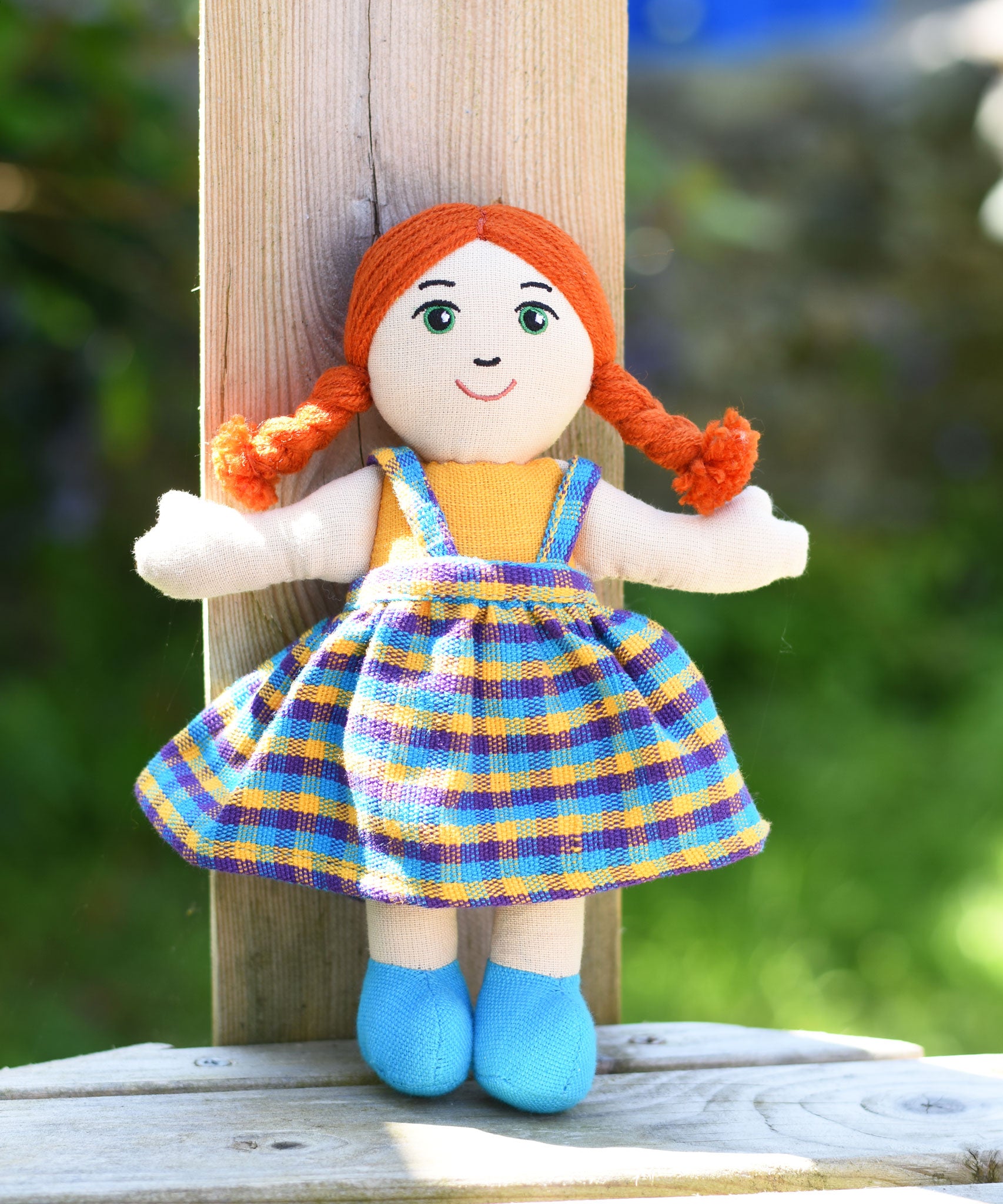 A Lanka Kade Girl Doll with White Skin and Red Hair leaning against a wooden post outdoors.