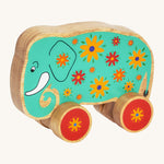 A green wooden Lanka Kade push along elephant with yellow and red flowers with red wheels on a cream background.