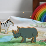 A Lanka Kade Grey Rhino Wooden Wild Animal Figure placed on a Wonderie Plains of Africa play cloth. An elephant and zebra figure can be seen in the background. 
These wooden toy figures are part of a huge range of Lanka Kade fair trade, wooden toys available here at Babipur.