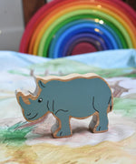 A Lanka Kade Grey Rhino Wooden Wild Animal Figure placed on a Wonderie Plains of Africa play cloth. A Grimm's rainbow can be seen in the background. These wooden toy figures are part of a huge range of Lanka Kade fair trade, wooden toys available here at Babipur.