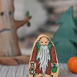 A Lanka Kade Brown & Green Wooden Hermit Figure placed in front of wooden toy trees. 