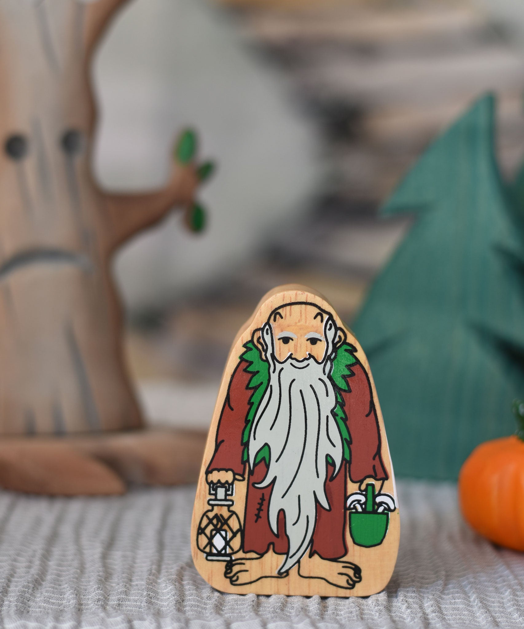 A Lanka Kade Brown & Green Wooden Hermit Figure placed in front of wooden toy trees. 