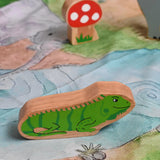 A Lanka Kade green iguana wooden toy figure placed on a Wonderie play cloth with a Babipur Lanka Kade mushroom in the background. These wooden toy figures are part of a huge range of Lanka Kade fair trade, wooden toys available here at Babipur.