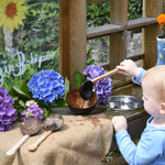 A child using the Lanka Kade cocnut shell ladle spoon to transfer water from a metal bowl into the coconut bowl. 