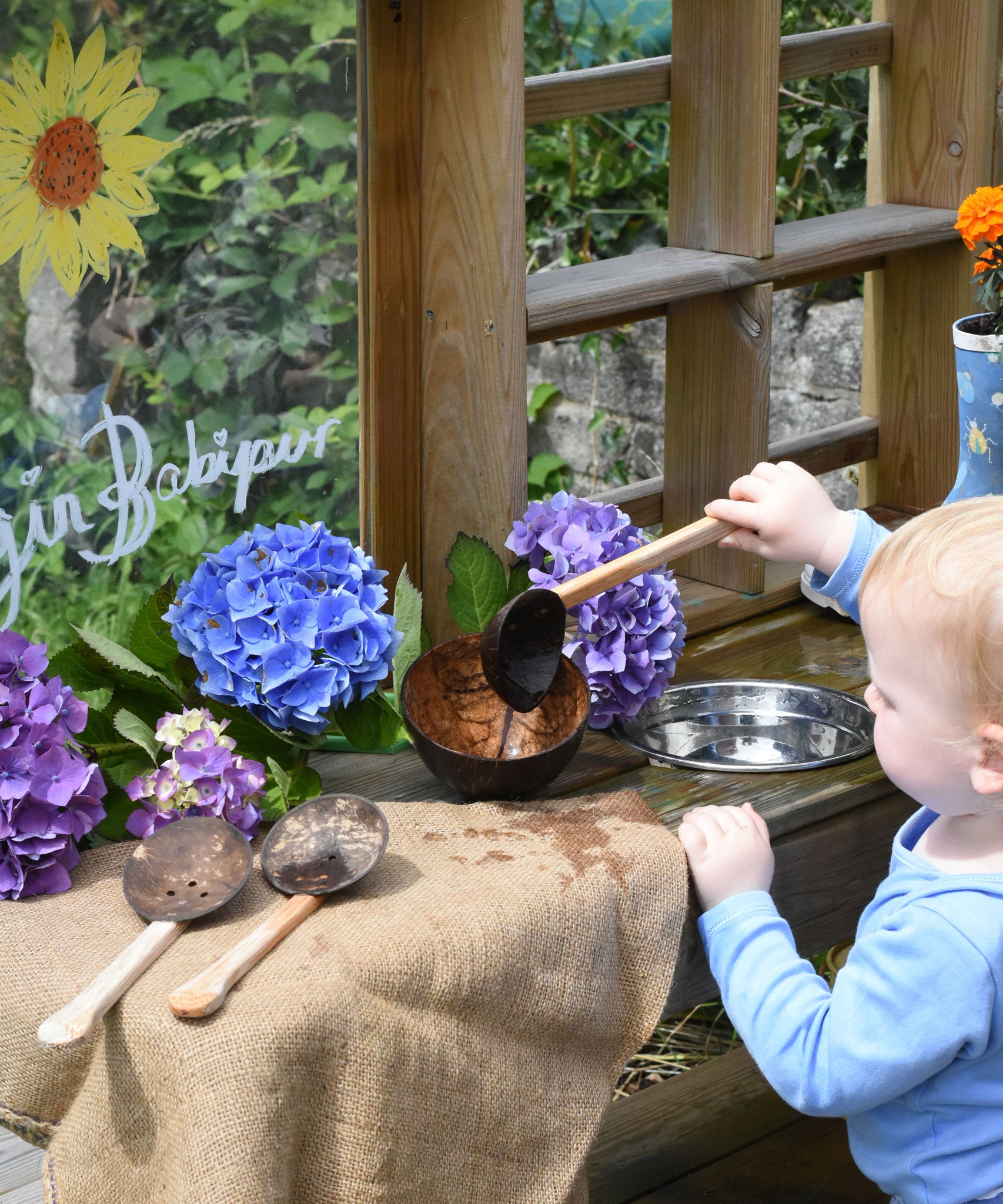 A child using the Lanka Kade cocnut shell ladle spoon to transfer water from a metal bowl into the coconut bowl. 