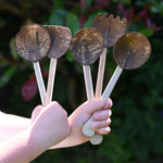 A child holding up the Lanka Kade Sri Lankan Coconut Shell Kitchen Utensils Playset in their hands. The set consists of 5 different coconut shell utensils on wooden handles.