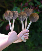 A child holding up the Lanka Kade Sri Lankan Coconut Shell Kitchen Utensils Playset in their hands. The set consists of 5 different coconut shell utensils on wooden handles.