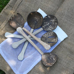 The 5 utensils from the Lanka Kade Coconut Shell Utensil Playset laid out on top of the mesh storage bag that they are supplied in. 