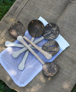 The 5 utensils from the Lanka Kade Coconut Shell Utensil Playset laid out on top of the mesh storage bag that they are supplied in. 