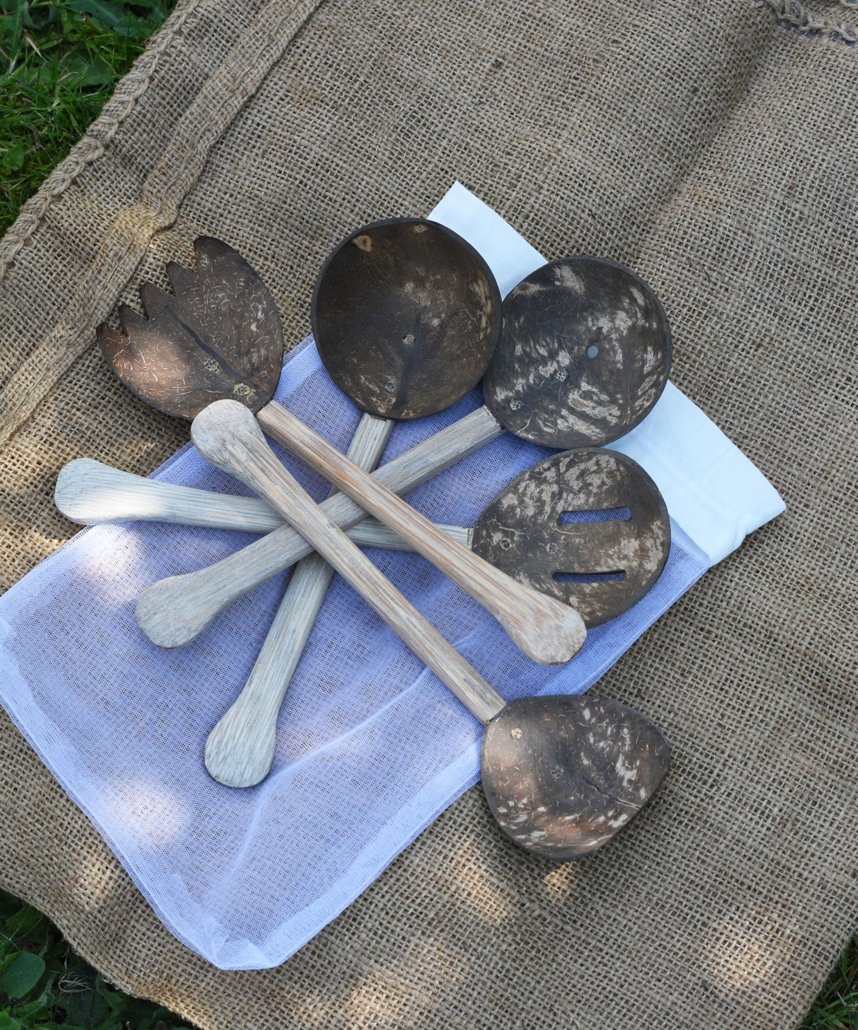 The 5 utensils from the Lanka Kade Coconut Shell Utensil Playset laid out on top of the mesh storage bag that they are supplied in. 