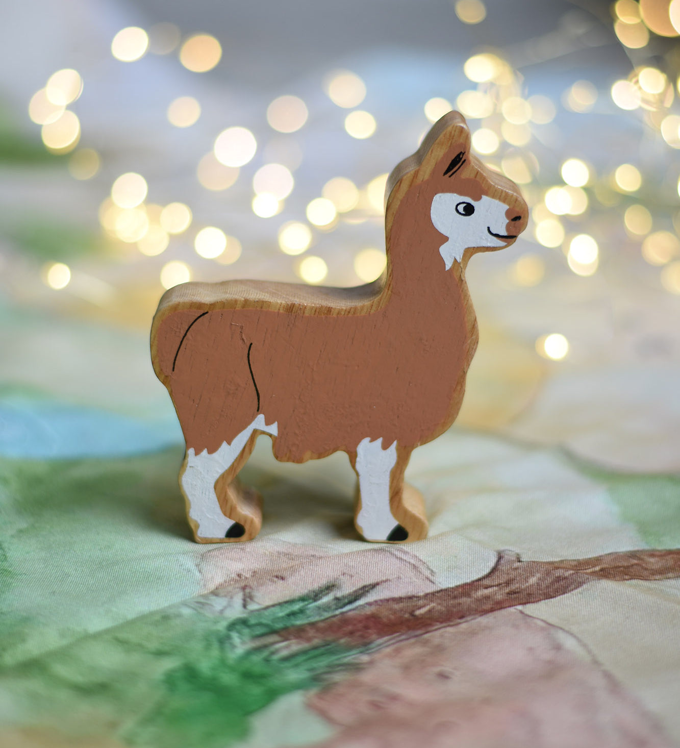 A Lanka Kade brown and white Llama wooden toy figure placed on a Wonderie play cloth. These wooden toy figures are part of a huge range of Lanka Kade fair trade, wooden toys available here at Babipur.