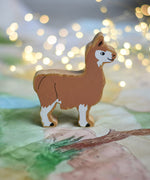 A Lanka Kade brown and white Llama wooden toy figure placed on a Wonderie play cloth. These wooden toy figures are part of a huge range of Lanka Kade fair trade, wooden toys available here at Babipur.