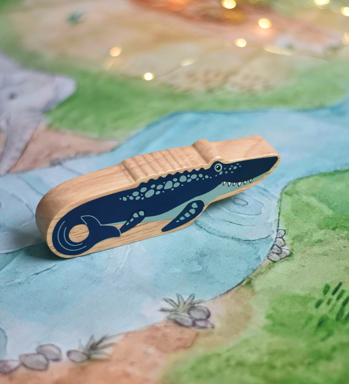 A Lanka Kade mosasurus wooden toy figure placed on a Wonderie plains of Africa play cloth. These wooden toy figures are part of a huge range of Lanka Kade fair trade, wooden toys available here at Babipur.
