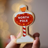 Lanka Kade red north pole sign wooden toy figure in an adult's hand.