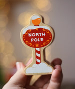 Lanka Kade red north pole sign wooden toy figure in an adult's hand.