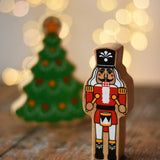 Lanka Kade nutcracker Christmas wooden toy figure placed on a wooden surface in the Babipur playroom with a Christmas tree in the background.