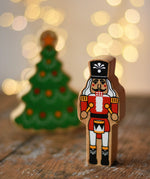 Lanka Kade nutcracker Christmas wooden toy figure placed on a wooden surface in the Babipur playroom with a Christmas tree in the background.