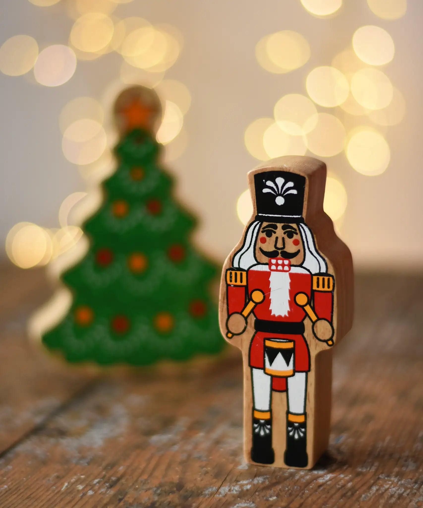 Lanka Kade nutcracker Christmas wooden toy figure placed on a wooden surface in the Babipur playroom with a Christmas tree in the background.