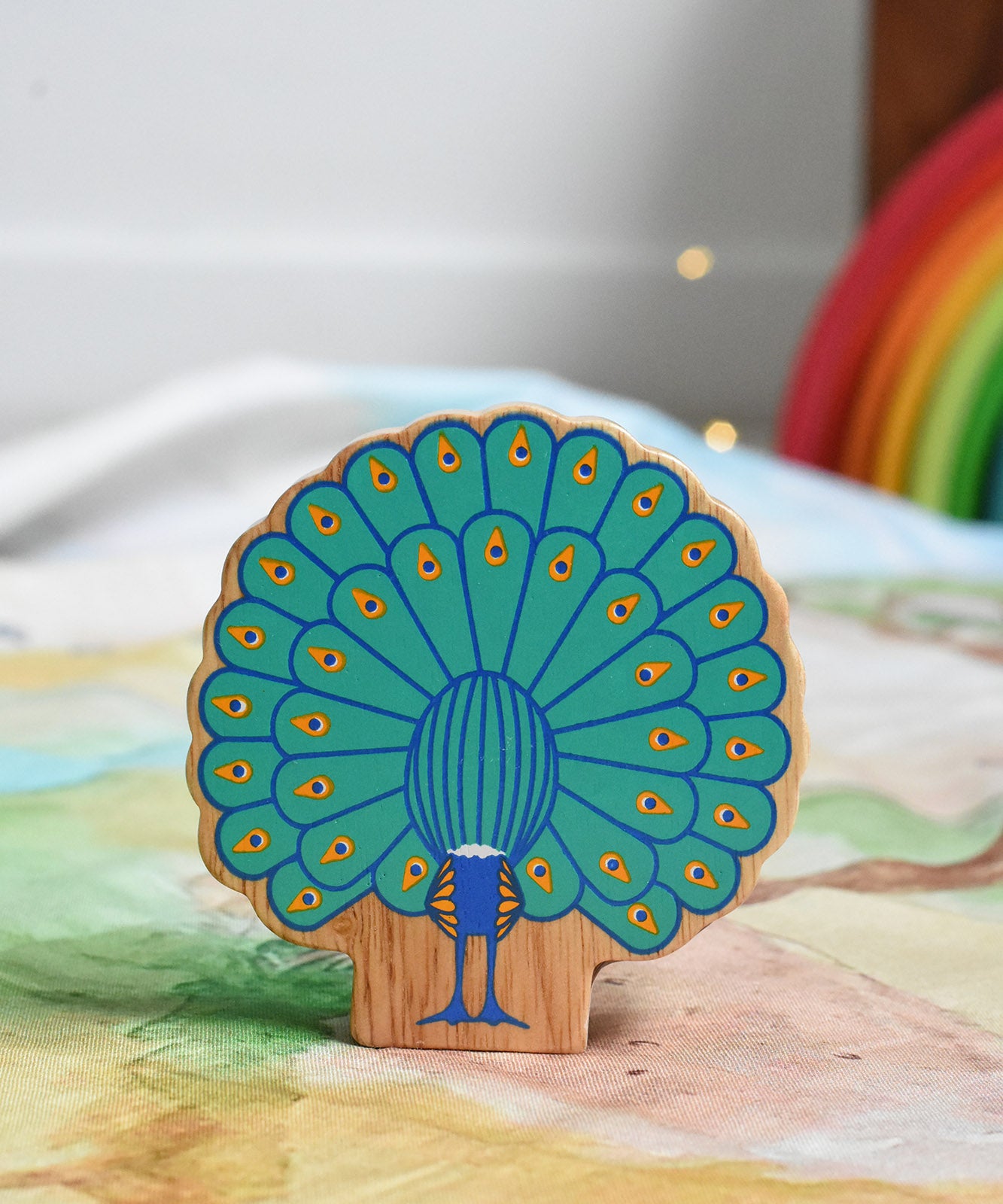 The back of a Lanka Kade peacock wooden toy figure placed on a Wonderie play cloth. The peacock toy has it's feather on display. These wooden toy figures are part of a huge range of Lanka Kade fair trade, wooden toys available here at Babipur.