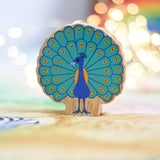 A Lanka Kade peacock wooden toy figure placed on a Wonderie play cloth. The peacock toy has it's feather on display. These wooden toy figures are part of a huge range of Lanka Kade fair trade, wooden toys available here at Babipur.