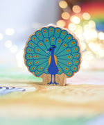 A Lanka Kade peacock wooden toy figure placed on a Wonderie play cloth. The peacock toy has it's feather on display. These wooden toy figures are part of a huge range of Lanka Kade fair trade, wooden toys available here at Babipur.