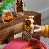 A child walking the cave man figure from the Lanka Kade Prehistoric Playset over a Grimm's wooden rainbow. A play set that contains 8 wooden figure and scenery pieces. These wooden toy figures are part of a huge range of Lanka Kade fair trade, wooden toys available here at Babipur.
