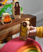 A child walking the cave man figure from the Lanka Kade Prehistoric Playset over a Grimm's wooden rainbow. A play set that contains 8 wooden figure and scenery pieces. These wooden toy figures are part of a huge range of Lanka Kade fair trade, wooden toys available here at Babipur.