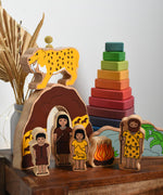 The Lanka Kade Prehistoric Playset set up on a small wooden table, a Grimm's Wankel stacking toy can be seen in the background. A play set that contains 8 wooden figure and scenery pieces. These wooden toy figures are part of a huge range of Lanka Kade fair trade, wooden toys available here at Babipur.