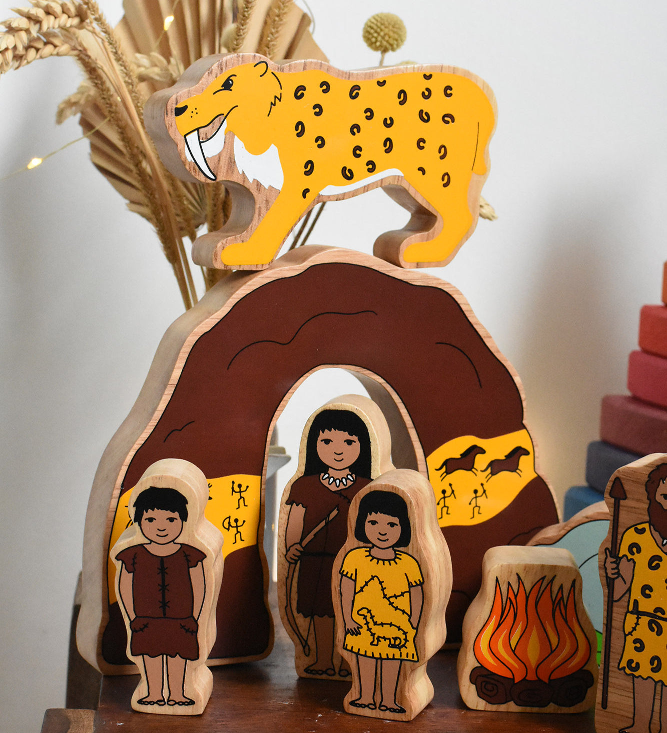 The Lanka Kade Prehistoric Playset set up on a small wooden table. A play set that contains 8 wooden figure and scenery pieces. These wooden toy figures are part of a huge range of Lanka Kade fair trade, wooden toys available here at Babipur.