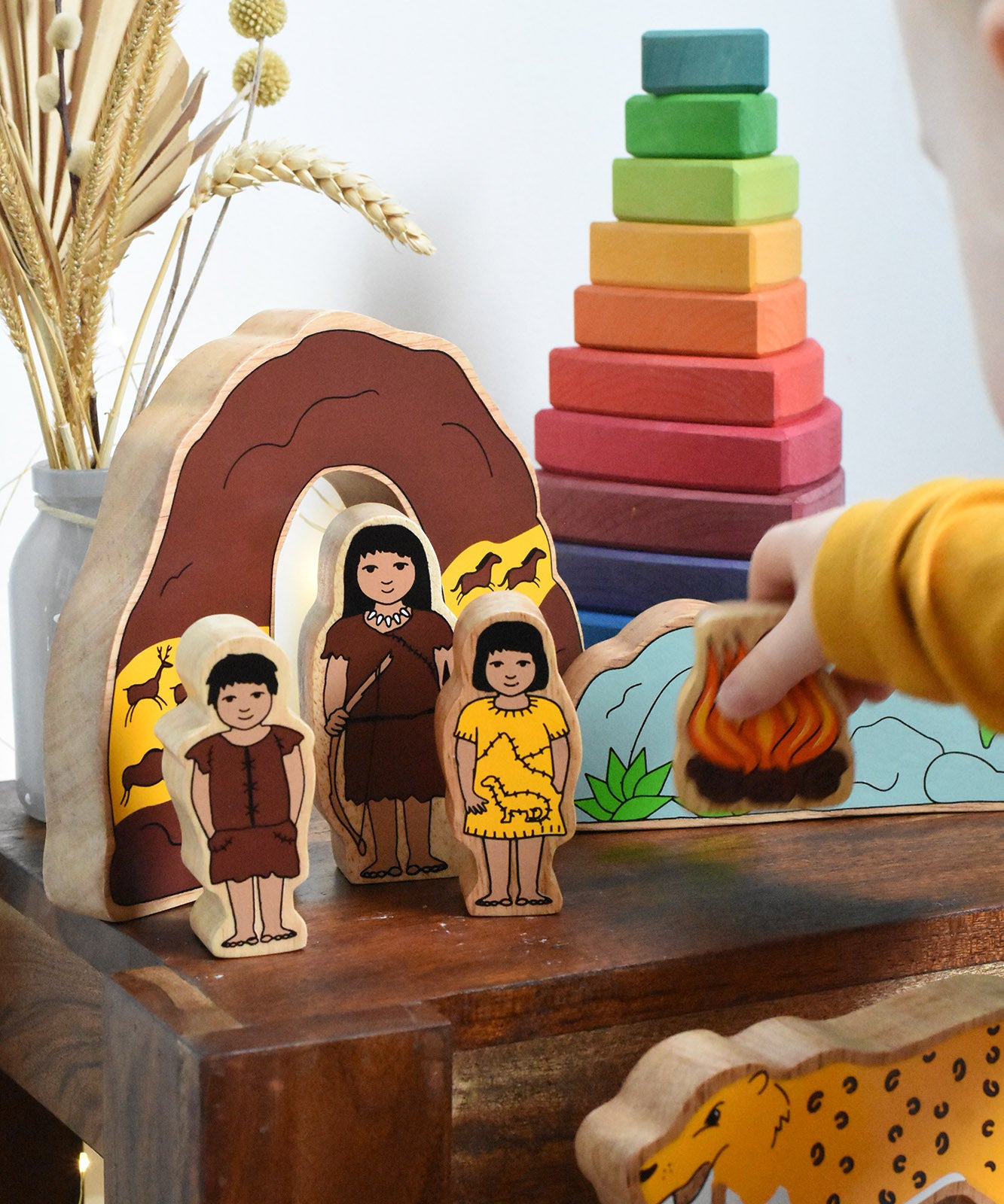 A child holding the fire from the Lanka Kade Prehistoric Playset. A play set that contains 8 wooden figure and scenery pieces. These wooden toy figures are part of a huge range of Lanka Kade fair trade, wooden toys available here at Babipur.