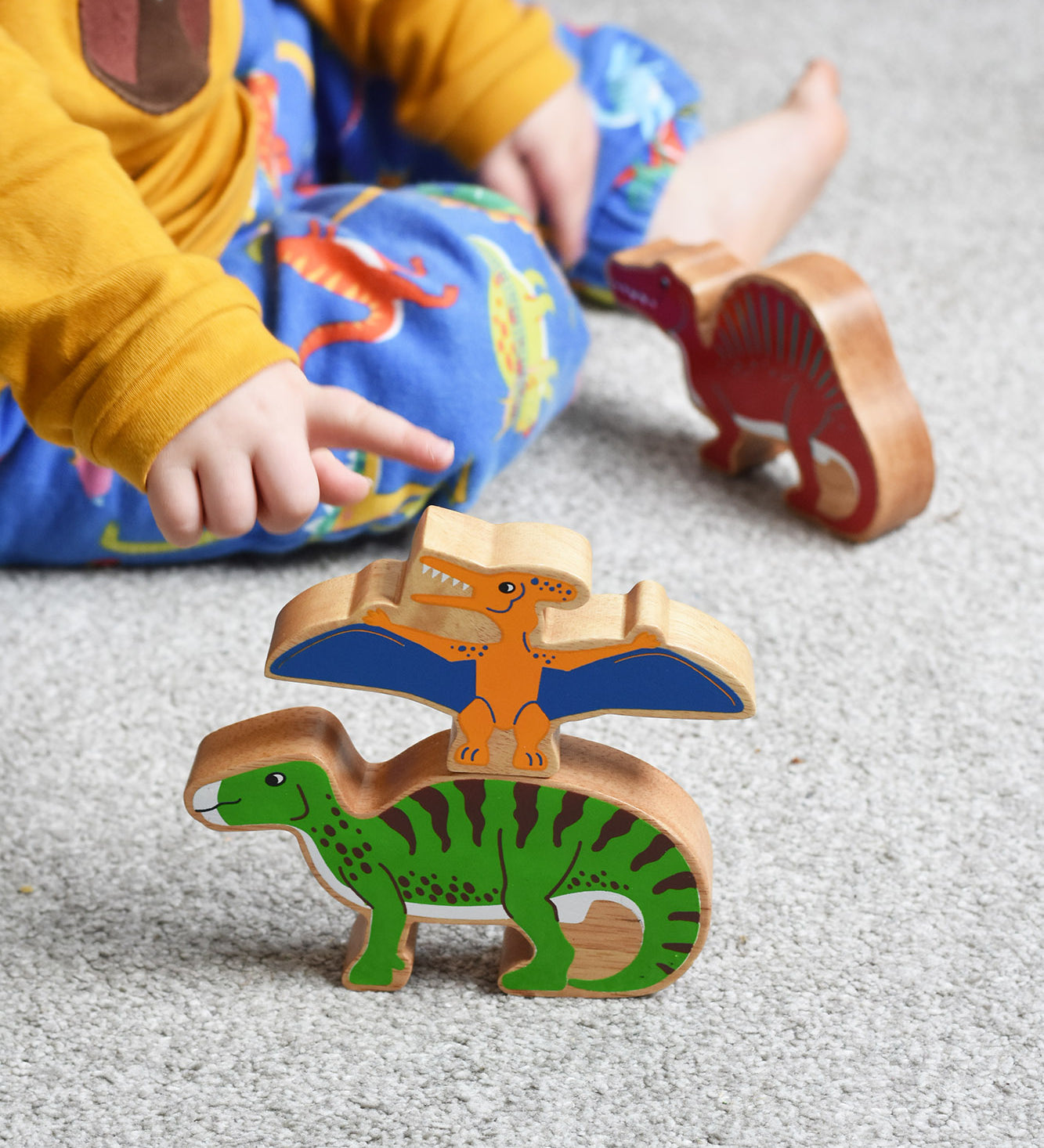 A child playing with Lanka Kade wooden toy dinosaur figures. The child is pointing at the Lanka Kade pteranodon figure. These wooden toy figures are part of a huge range of Lanka Kade fair trade, wooden toys available here at Babipur.