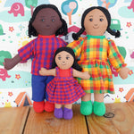 A Lanka Kade Fair Trade Rag Doll Dad with black Skin and black hair, Mum with brown skin and black hair and daughter with brown skin and black hair. The rag dolls are in a standing position on a wooden surface. 