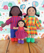 A Lanka Kade Fair Trade Rag Doll Dad with black Skin and black hair, Mum with brown skin and black hair and daughter with brown skin and black hair. The rag dolls are in a standing position on a wooden surface. 