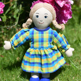A Lanka Kade Rag Doll Mum with White Skin and Blonde Hair placed on grass in front of peonies growing in a garden.