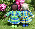 Two Lanka Kade Rag Doll Mums one with black hair and black skin White Skin, Blonde Hair placed on grass in front of peonies growing in a garden.