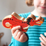 Lanka Kade wooden toy dragon figure in red with black, white and orange details in a child's hand. The child can be seen looking on in the background.