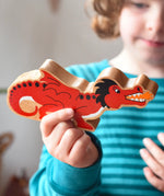 Lanka Kade wooden toy dragon figure in red with black, white and orange details in a child's hand. The child can be seen looking on in the background.