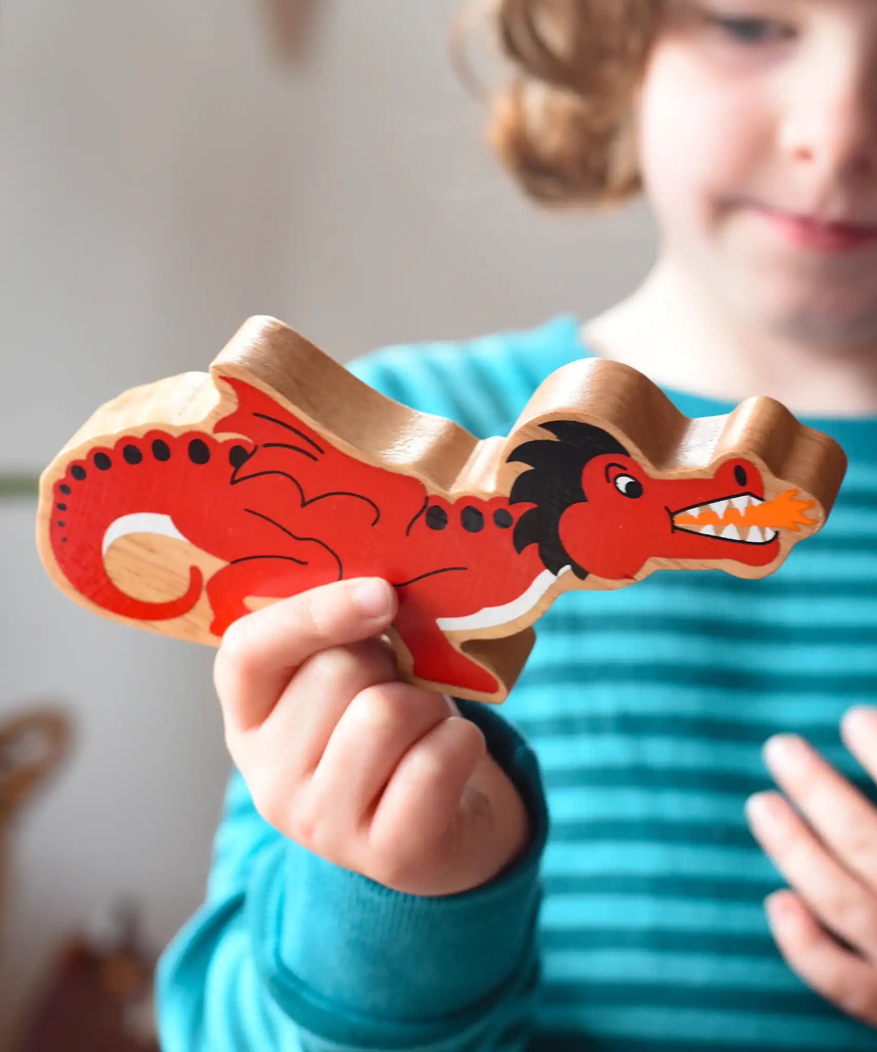 Lanka Kade wooden toy dragon figure in red with black, white and orange details in a child's hand. The child can be seen looking on in the background.