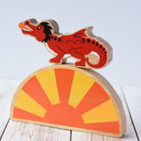 Lanka Kade red dragon wooden toy dragon figure with black details placed on a yellow and orange Babipur sun arch placed on a wooden surface. 