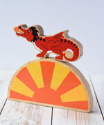 Lanka Kade red dragon wooden toy dragon figure with black details placed on a yellow and orange Babipur sun arch placed on a wooden surface. 