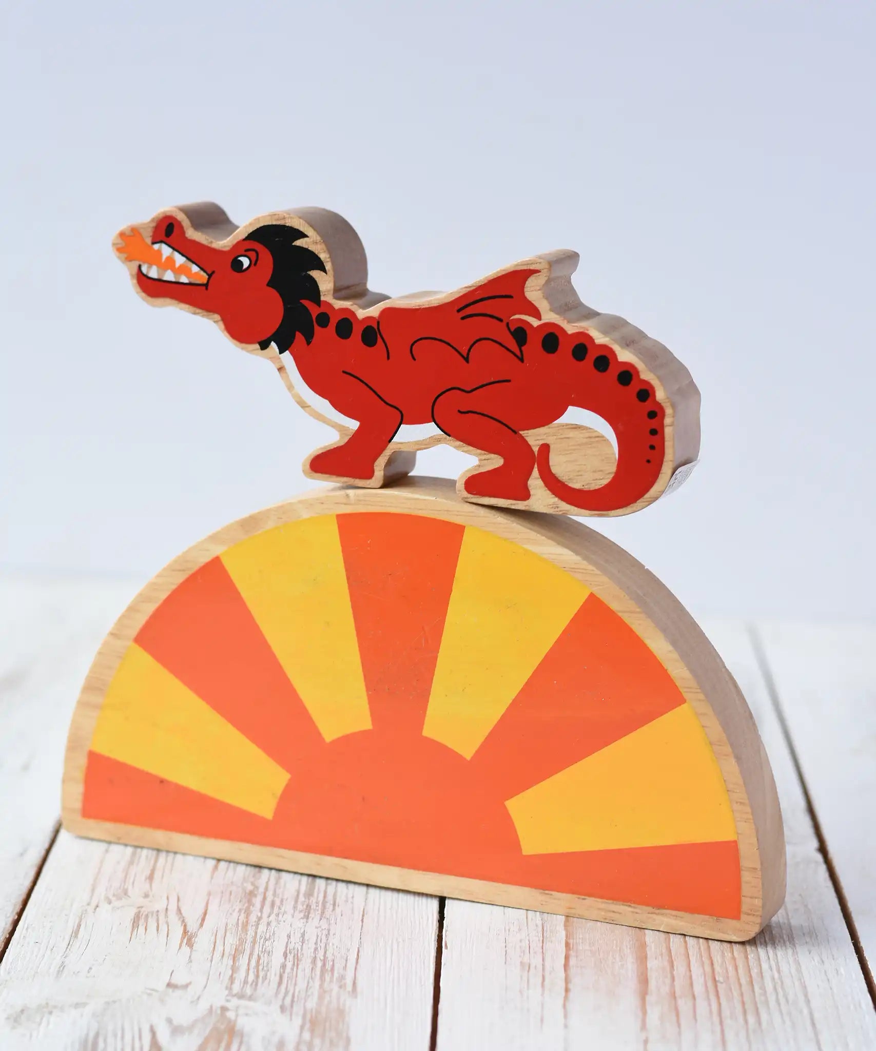 Lanka Kade red dragon wooden toy dragon figure with black details placed on a yellow and orange Babipur sun arch placed on a wooden surface. 