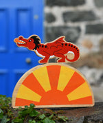 Lanka Kade red dragon wooden toy dragon figure with black details placed on a yellow and orange Babipur sun. 