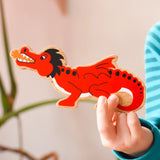 Lanka Kade wooden toy dragon figure in red with black, white and orange details in a child's hand. 