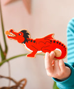 Lanka Kade wooden toy dragon figure in red with black, white and orange details in a child's hand. 