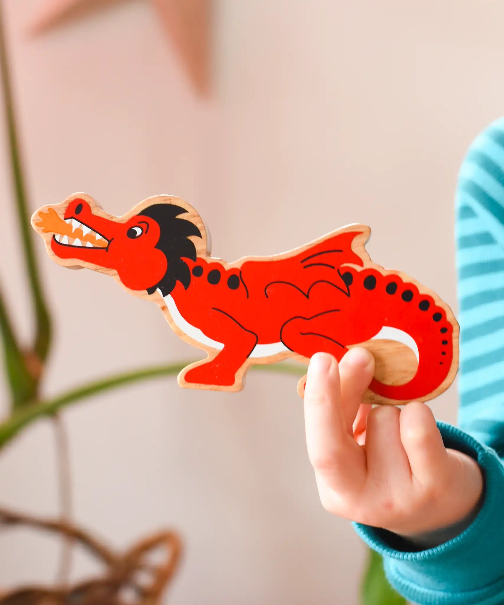 Lanka Kade wooden toy dragon figure in red with black, white and orange details in a child's hand. 