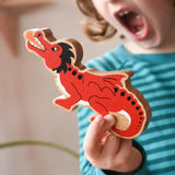 Lanka Kade wooden toy dragon figure in red with black, white and orange details in a child's hand. The child can be seen roaring in the background.