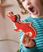 Lanka Kade wooden toy dragon figure in red with black, white and orange details in a child's hand. The child can be seen roaring in the background.
